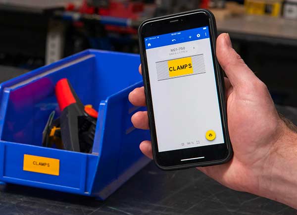 En etikettdesign på en Ekspressetiketter på mobil-skjerm ved siden av den faktiske etiketten som skrives ut. Begge er kraftig gule og har påskriften «CLAMPS».