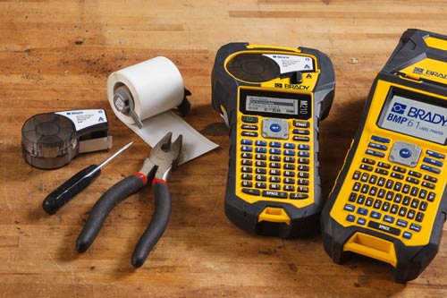 To kassetter med standardetiketter ved siden av en M210 og en M610 etikettskriver.