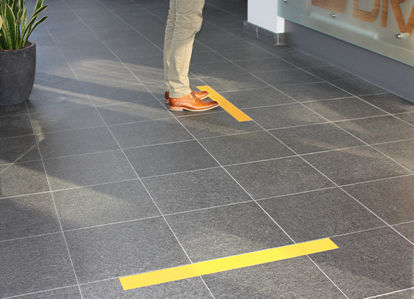 En person fjerner ToughStripe Vinyl gulvtape fra vinylkomposittfliser. Tapen løsner rent og i ett stykke.