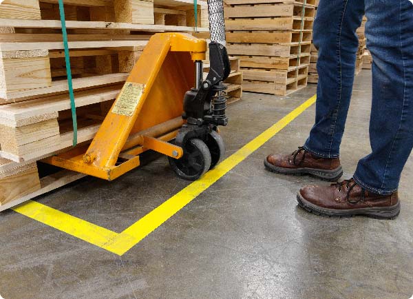 Kraftig gul ToughStripe gulvtape påført et lagergulv. Plasseringen viser hvor en jekketralleoperatør skal sette fra seg en pall med materialer.